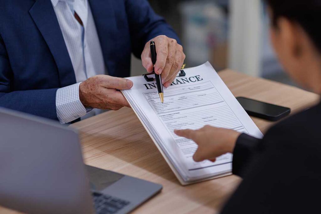 A person reviews health insurance documents at a kitchen table with a cup of coffee and a pen.