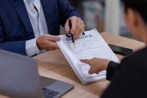 A person reviews health insurance documents at a kitchen table with a cup of coffee and a pen.